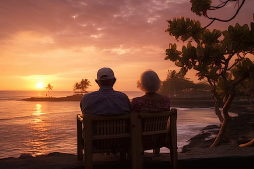 Silhouette of an elderly couple waiting for a colorful sunset sitting by the ocean.