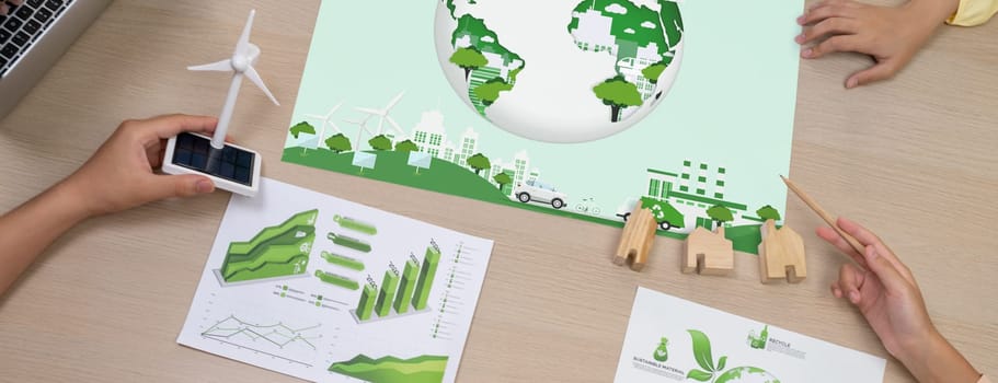 Green city poster was placed on green business meeting room. Professional architect hand holding wind mill model represented renewable energy. Green design. Closeup. Top view. Delineation.