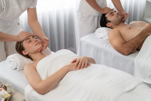 Caucasian couple enjoying relaxing anti-stress head massage and pampering facial beauty skin recreation leisure in dayspa modern light ambient at luxury resort or hotel spa salon. Quiescent