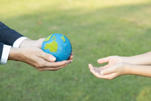 Businessman hand giving Earth globe to little boy as Earth day concept as corporate social responsible to contribute greener environmental protection for sustainable future generation. Gyre