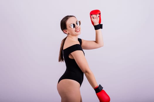 Seductive female boxer with athletic beautiful figure in black swimsuit gloves on a gray background