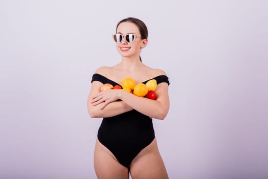 A female holding an apples, lemons, oranges in different arms isolated on grey background.