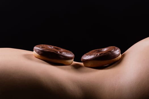 Close up shot of nude woman's body with chocolate covered donuts