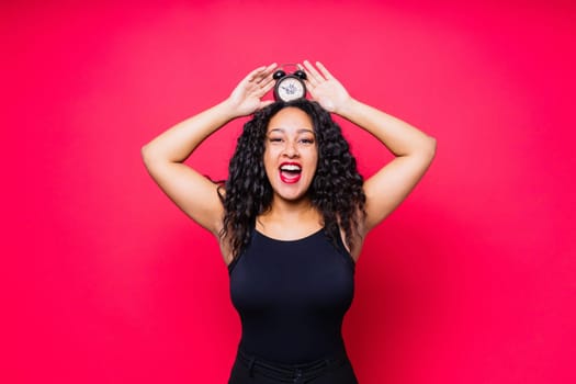 Smiling young african american woman posing isolated on a red background with clock