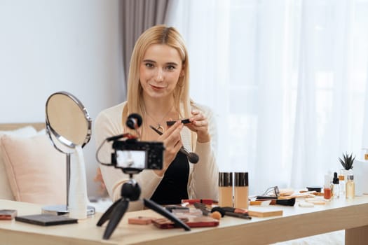 Young woman making beauty and cosmetic tutorial video content for social media. Beauty blogger smiles to camera while showing how to beauty care to audience or followers. Blithe