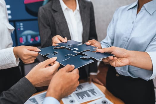 Corporate officer worker collaborate in office, connecting puzzle pieces with report paper on table as partnership and teamwork. Unity and synergy in business concept by merging jigsaw puzzle. Concord