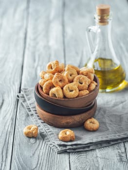 Traditional italian snack taralli or tarallini in wooden bowl over old gray wooden table. Rustic shot of taralli appetizer with copy space. Vertical.