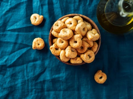 Traditional italian snack taralli or tarallini in wooden bowl over dark blue linen napkin background. Rustic shot of taralli appetizer with copy space. Top view or flat lay.
