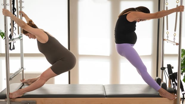 Two pregnant women are doing Pilates on a Cadillac reformer