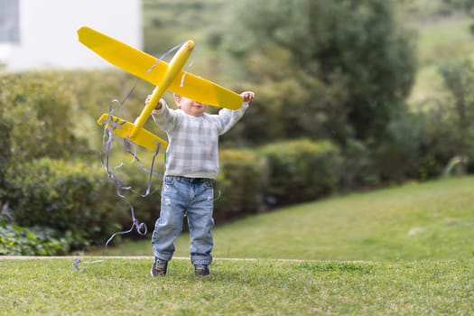 Boy toddler plays with toy model of airplane in park - telephoto