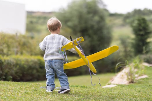 Boy toddler plays with toy airplane in park - telephoto