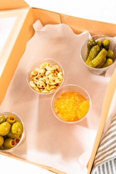 In the process of assembling, a woman expertly curates this charcuterie box, showcasing sliced meat, cheese, crackers, and grapes, all neatly arranged and packaged in a brown gifting box.