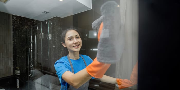 Cleaning online service. yong woman housekeeper cleaning bathroom mirror with cloth. House cleaning service concept.