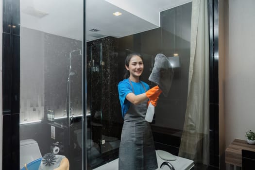 Cleaning online service. yong woman housekeeper cleaning bathroom mirror with cloth. House cleaning service concept.