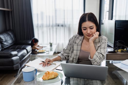 Business woman working from home and taking care of child while working, child doing activities in the background.