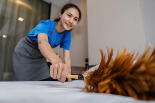 A woman is cleaning a bed with a feather duster. She is wearing a blue shirt and orange gloves