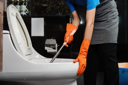 Cleaning online service. yong woman housekeeper cleaning flush toilet in bathroom with toilet brush. House cleaning service concept.