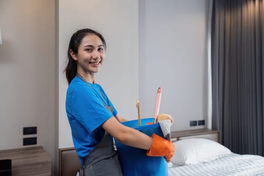 A woman in a blue shirt is holding a bucket with cleaning supplies. She is smiling and she is happy
