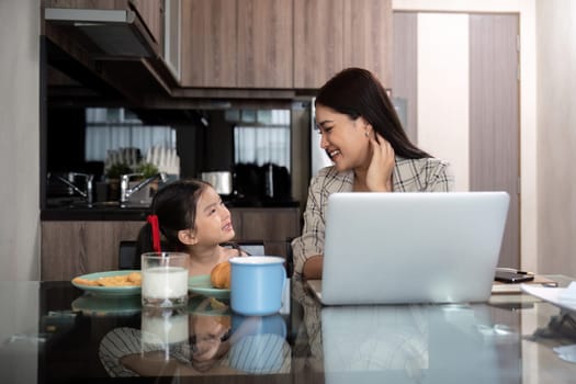 Working mom work from home office. Happy mother and daughter look to each other. businesswoman and cute child using laptop work freelancer workplace in cozy kitchen, Lifestyle.