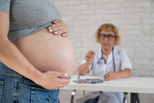 Doctor obstetrician gynecologist at his desk in the background. Close-up of a pregnant woman's belly