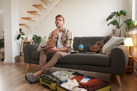 Portrait of traveller preparing for another journey, tourist packs suitcase with clothes for holiday, going on vacation.