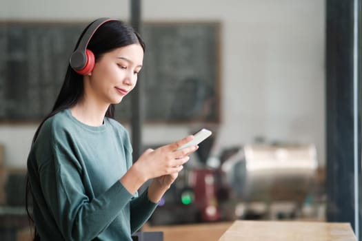 A woman wearing headphones is looking at her phone. She is smiling and she is enjoying herself