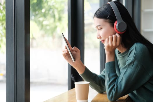 A woman is sitting at a table with a tablet in front of her. She is wearing headphones and she is enjoying her music