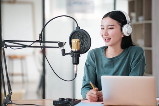 A woman is sitting at a desk with a microphone and a laptop. She is smiling and she is happy