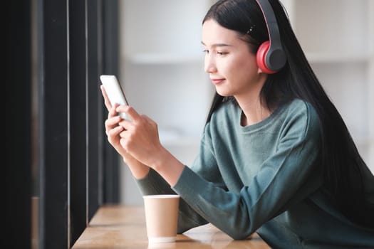 A woman is sitting at a table with a cup of coffee and a cell phone. She is wearing headphones and she is listening to music