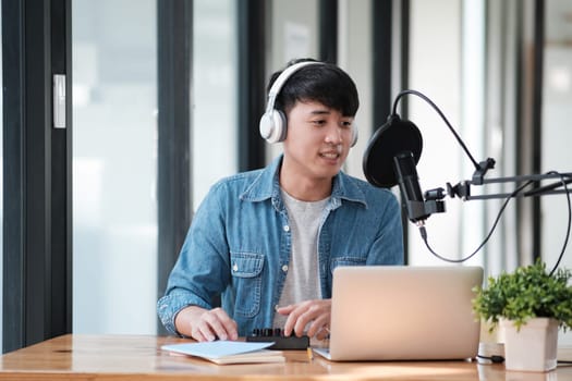 A man wearing headphones is sitting at a desk with a laptop and a microphone. He is likely recording a podcast or a voiceover
