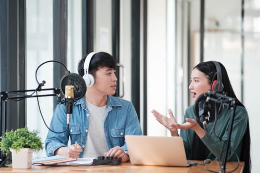 Two people are talking on a microphone. One of them is wearing headphones. The other person is looking at the camera