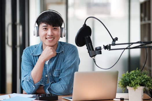 A man wearing headphones is smiling and sitting in front of a laptop. He is likely a radio host or a podcast host