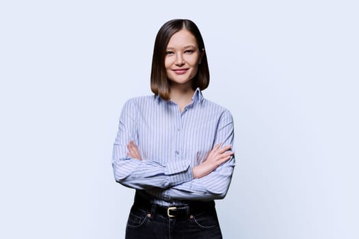 Young confident smiling business woman with crossed arms on white studio background. Positive happy female in shirt, student worker owner entrepreneur looking at camera. Business work education people