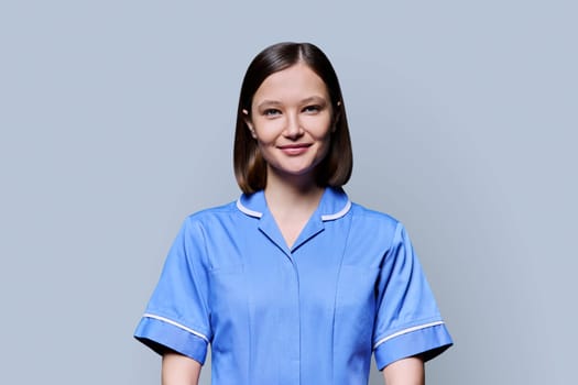 Portrait of young confident smiling female nurse looking at camera on gray studio background. Medical services, health, professional assistance, medical care concept