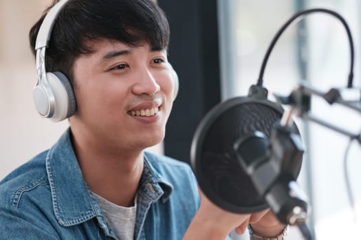 A man wearing headphones is smiling while holding a microphone. He is in a recording studio. Scene is cheerful and positive