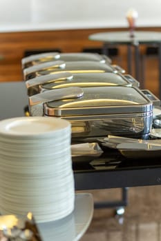 Row of closed chafing dishes at party banquet hall. Marmites ready for service made of stainless steel at buffet.