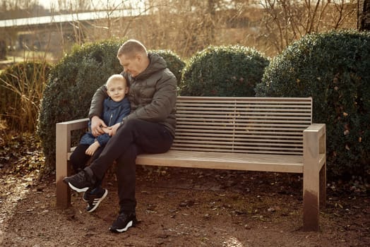 Autumnal Family Affection: Father, 40 Years Old, and Son - Beautiful 8-Year-Old Boy, Seated in the Park. Embrace the warmth of familial love in the autumnal air with this heartwarming image. A father, 40 years old, and his son - a beautiful 8-year-old boy, seated in the park. The essence of autumn adds a touch of seasonal charm to this delightful moment of family affection.