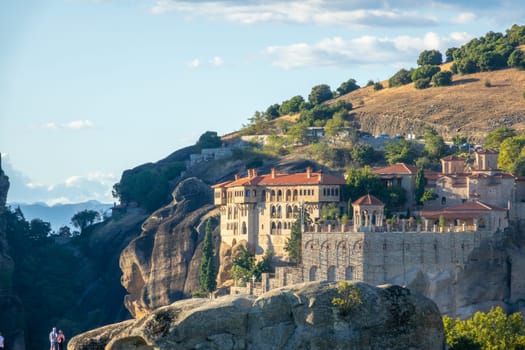 Greece. Sunny summer day in Meteora. Tourists look at a large rock monastery near a green hill