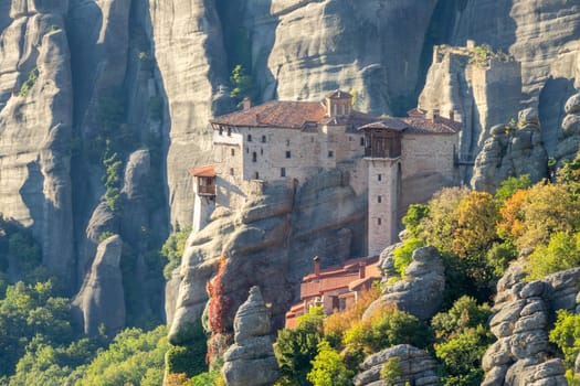 Greece. Sunny summer evening in the mountain valley of Meteora. Monastery on top of a cliff with a large mountain in the background