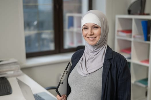 Pregnant Caucasian woman in hijab working in the office