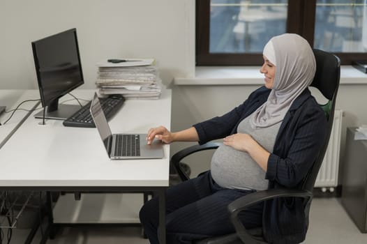 Pregnant Caucasian woman in hijab working at a computer in the office