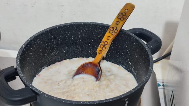 cooked oatmeal, wooden spoon, cooking food breakfast carbohydrates, black pan. High quality photo