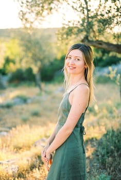 Smiling young woman stands half-turned near a tree. High quality photo