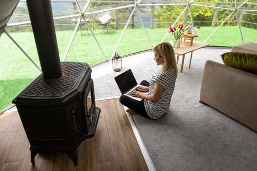 middle aged woman uses a laptop resting and spending time at Glamping house on holidays. holiday dome tent. Cozy, camping, hygge, lifestyle concept.