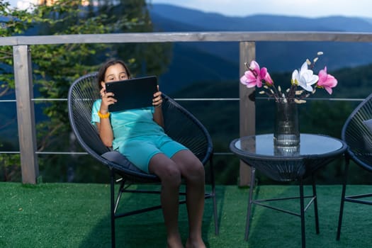 Little girl uses a tablet on the terrace.