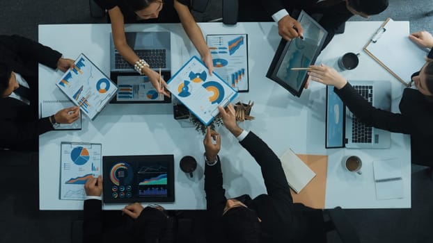 Top down aerial view of business people discussing about financial strategy on table with document and tablet display investment statistic at meeting. Diverse team brainstorm about plan. Directorate.