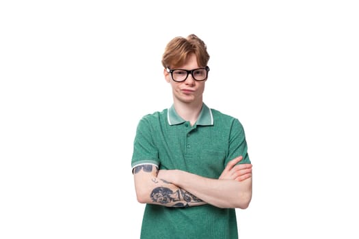young red-haired man in a green t-shirt stands thoughtfully on a white background with copy space.