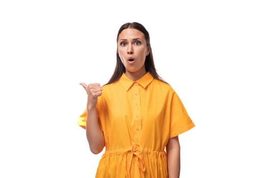 young brunette woman dressed in a summer yellow dress points her finger to the side in surprise.