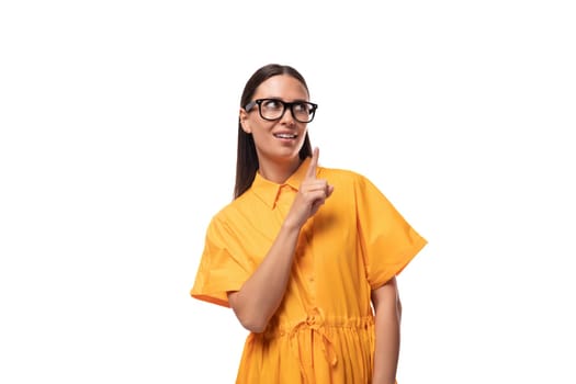 a young well-groomed woman with black straight hair dressed in a yellow dress points her finger to the side.