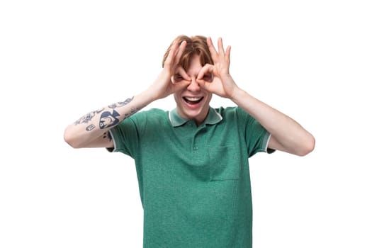 a young slender ginger man with a tattoo on his arm, dressed in a green T-shirt with bright facial expressions.